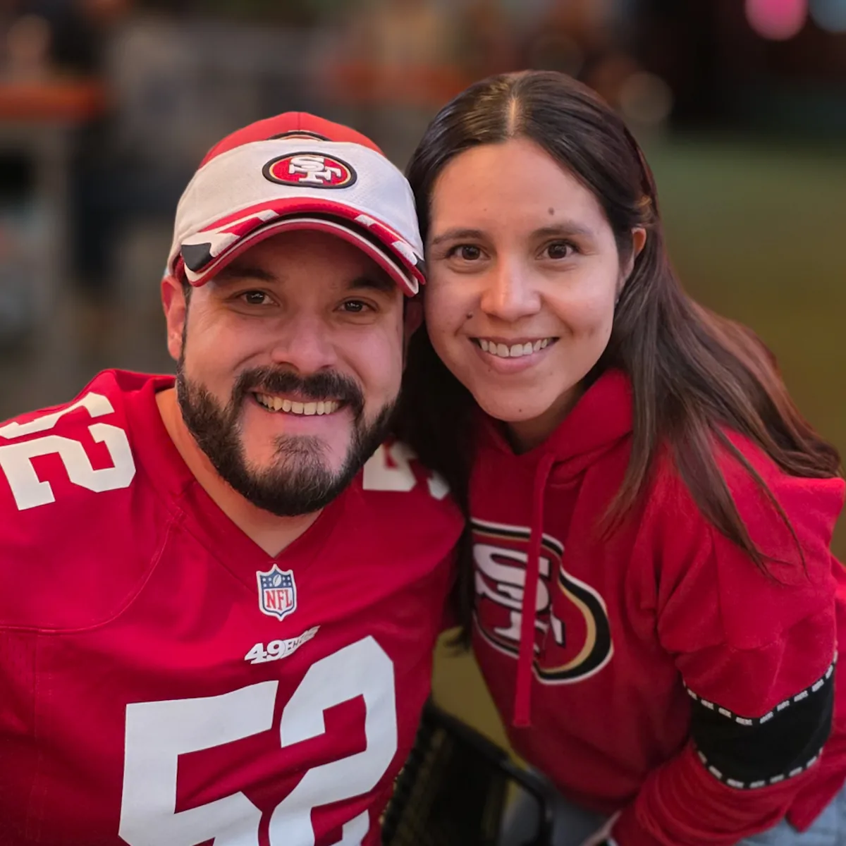 Pareja sonriendo con jersey 52 y sudadera roja de los 49ers