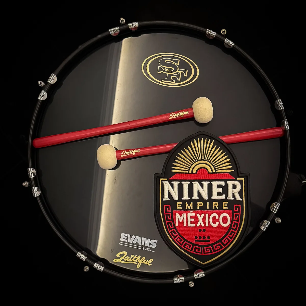 Acercamiento al bombo con el logo de los 49ers, el escudo de Niner Empire México y sus baquetas